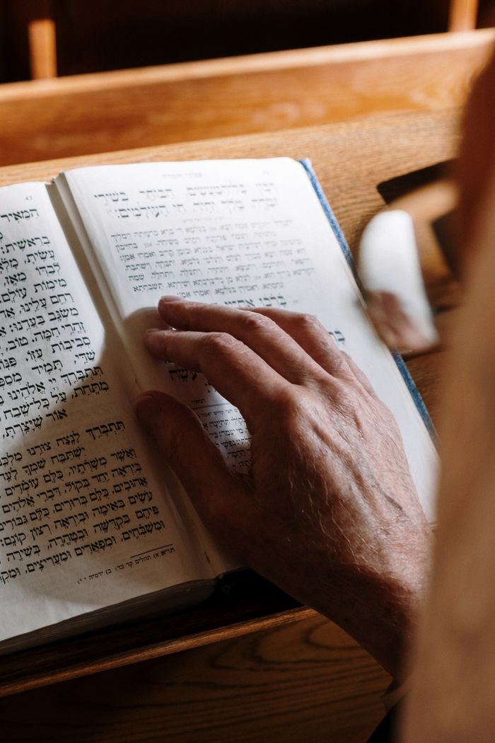Close-up of an elderly hand on a Hebrew Torah text in a synagogue setting.